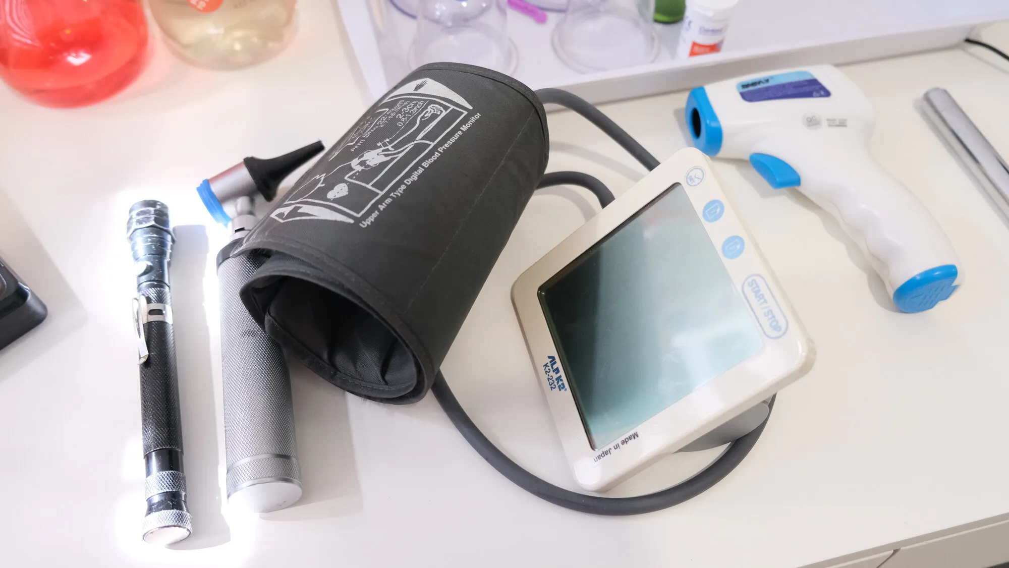 A blood pressure monitor, infrared thermometer, otoscope and glucometer laid out on the examination desk