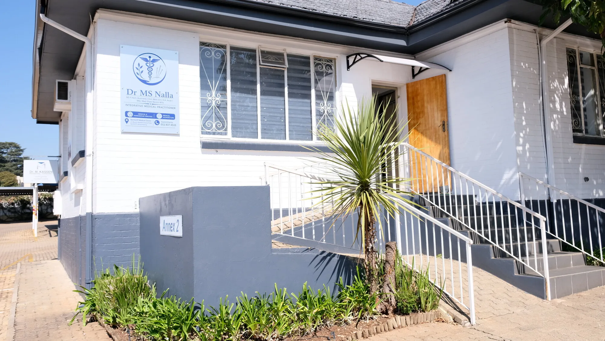 The entrance to the rooms: a white building with the Dr MS Nalla board beside the window, Annex 2 on the low wall, and a handrail up the steps to a wooden door